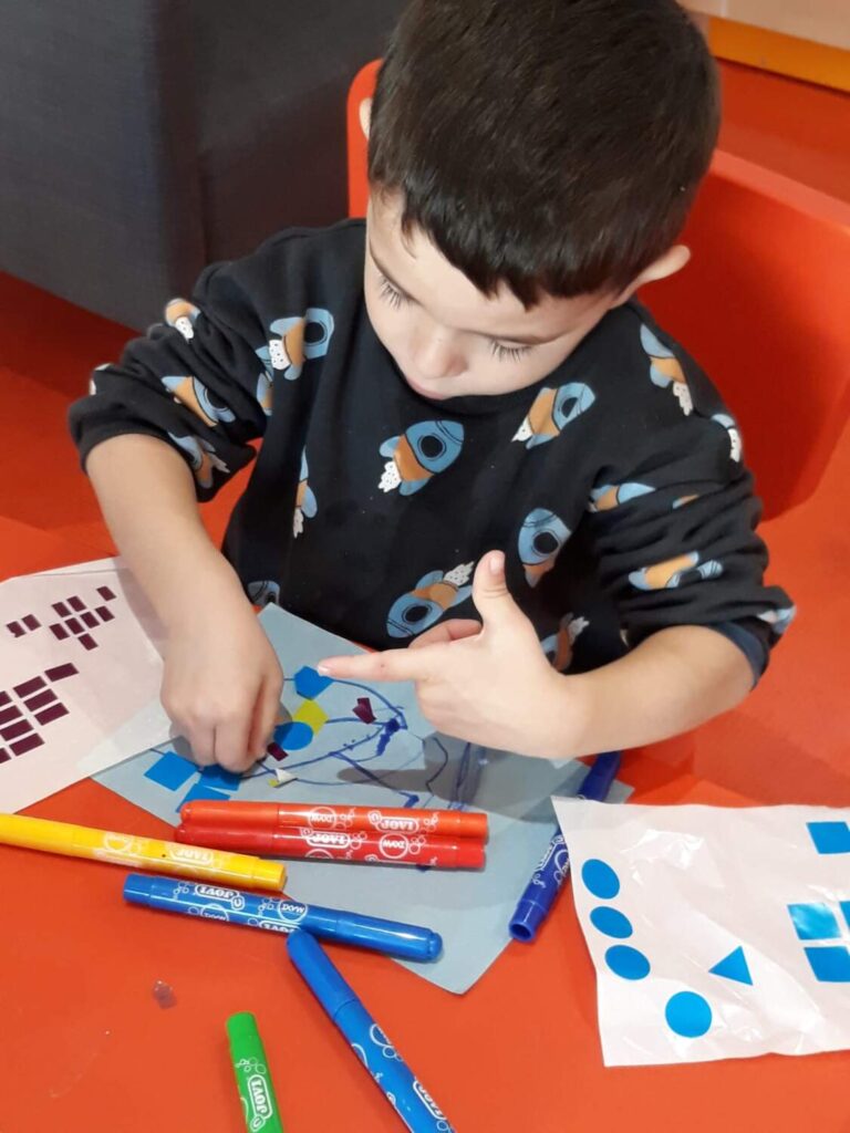 PHOTO D'UN PETIT GARÇON ENTRAIN DE COLLER DES PASTILLES SUR UNE FEUILLE