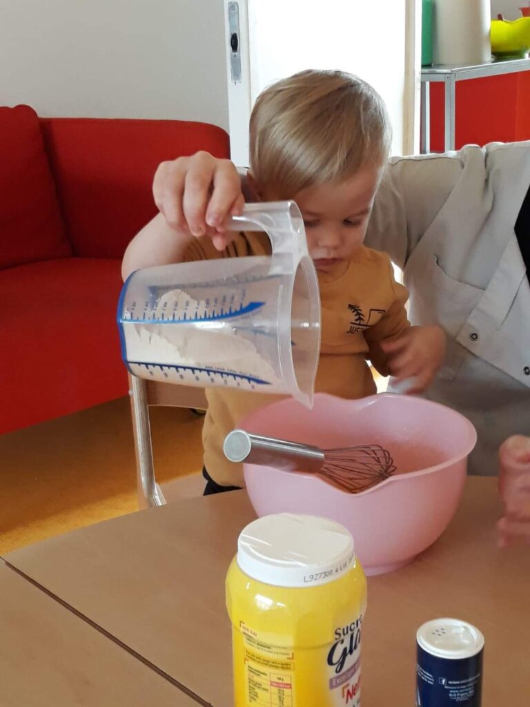 PHOTO D'U,N ENFANT ENTRAIN DE PRÉPARER UNE PÂTE À CRÊPE AVEC UNE ÉDUCATRICE