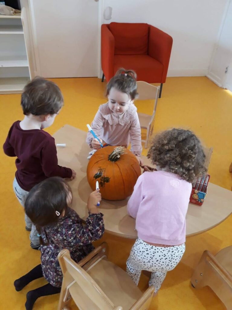 PHOTO DES ENFANTS DE LA CRÈCHE DES MINIS ENTRAIN DE DESSINER SUR UNE CITROUILLE POUR HALLOWEEN