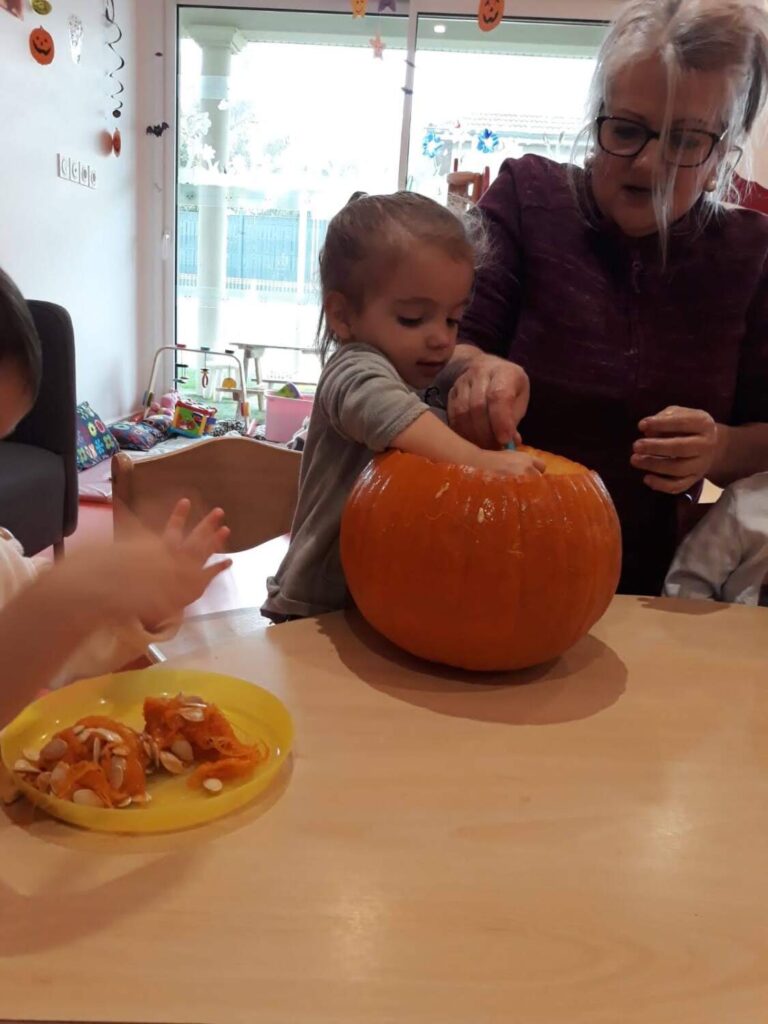 PHOTO D'UNE ÉDUCATRICE ET DES ENFANTS DE LA CRÈCHE DES MINIS ENTRAIN DE PRÉPARER UNE CITROUILLE POUR HALLOWEEN