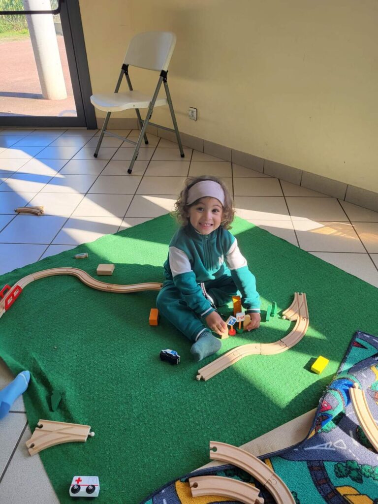 PHOTO D'UN ENFANT DE LA CRÈCHE DES MINIS ENTRAIN DE JOUER AVEC UN JEU DE TRAIN EN BOIS
