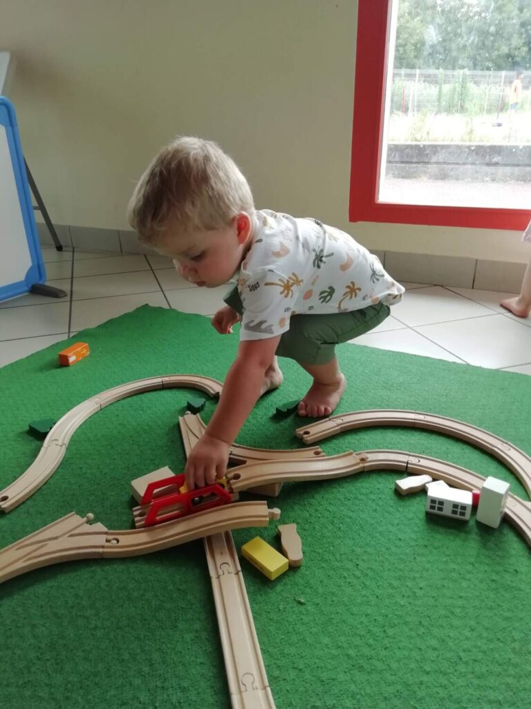 PHOTO D'UN PETIT GARÇON DE LA CRÈCHE ENTRAIN DE JOUER AVEC UN TRAIN EN BOIS