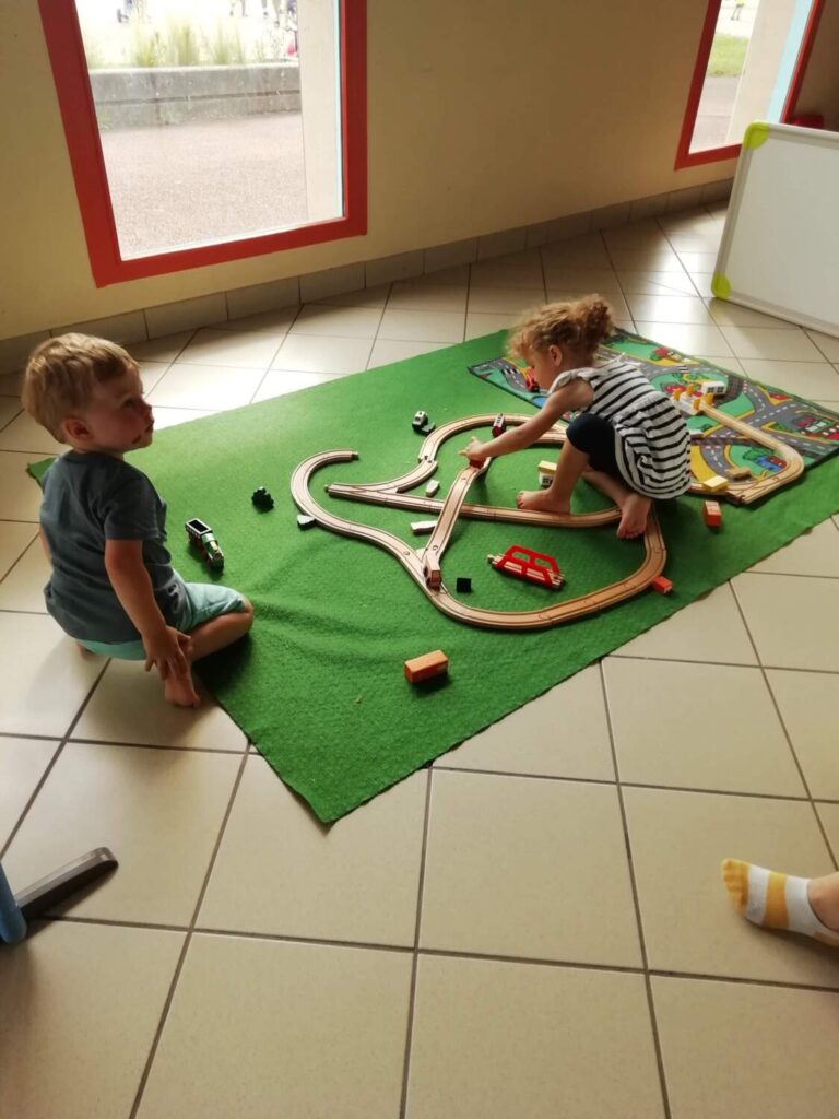 PHOTO DE DEUX ENFANTS DE LA CRÈCHE ENTRAIN DE JOUER AVEC UN TRAIN EN BOIS