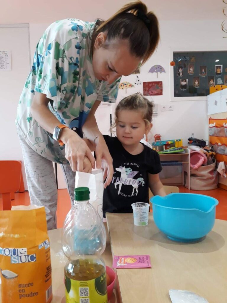 photo d'une éducatrice entrain d'aider une petite fille à préparer un gâteau